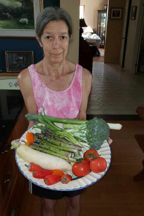 Jeannette holds a colourful vegetable platter with red tomatoes, green asparagus, a leek, broccoli, red peppers and white daikon radish.